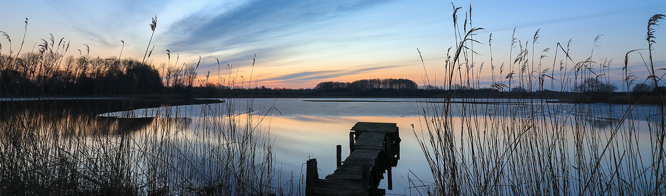 Winterlicher See mit Steg bei Sonnenaufgang vermittelt Ruhe und Besinnlichkeit zur Bestattungsvorsorge in Oberursel.