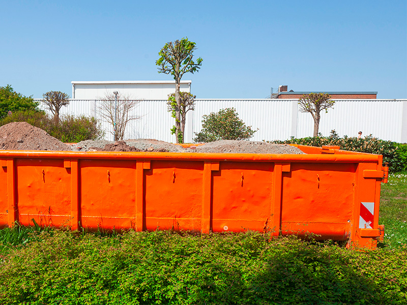 Orangener Container für Bauschutt steht auf einer Wiese in Deutschland zur Zwischenlagerung von Bauabfällen.