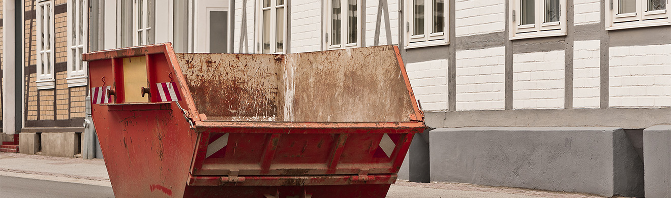 Roter Bauschuttcontainer steht vor Fachwerkhaus auf Baustelle für Abbruch- und Entsorgungsarbeiten im Außenbereich.