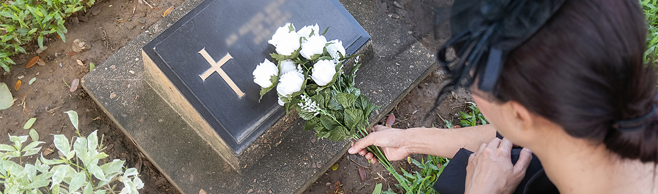 Junge Frau legt weiße Blumen auf ein Urnengrab auf einem gepflegten, grünen Friedhof als Zeichen des Gedenkens.